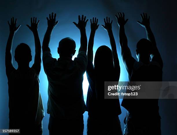 group of people silhouette. arms raised in praise. blue light. - cultus stockfoto's en -beelden