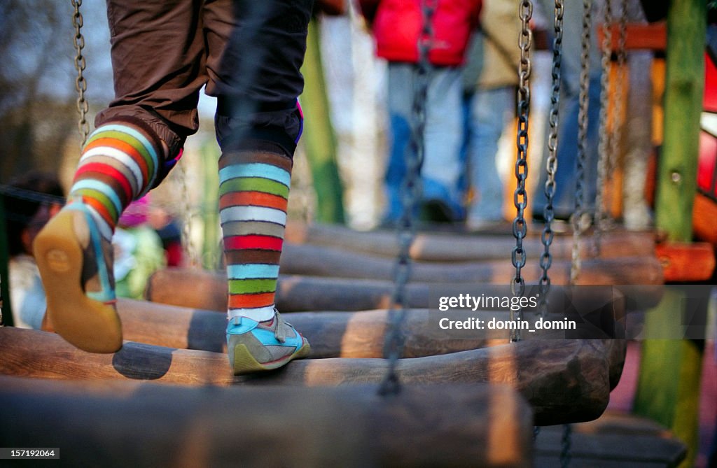 Girl is running through the wooden bridge on children playground