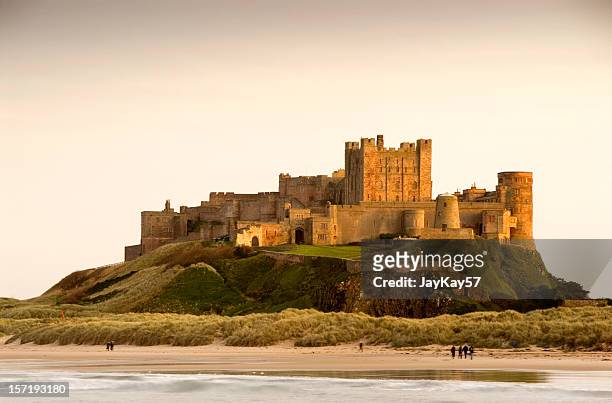 bamburgh castle daytime with people walking on beach - beach uk stockfoto's en -beelden
