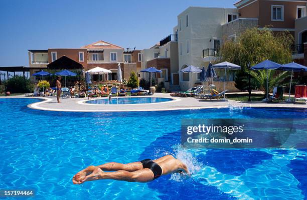 young man jumping into the hotel's pool located on backyard - kreta stockfoto's en -beelden