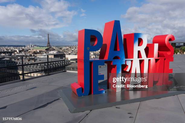 Sign which reads 'Paris I Love You' on the roof of the Galeries Lafayette department store, backdropped by the Eiffel Tower on the city skyline in...