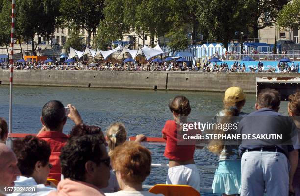 Tourists on a boat watch people enjoying the sun on the opening day of the fourth edition of Paris Plage, 21 July 2005 on the river Seine in Paris....