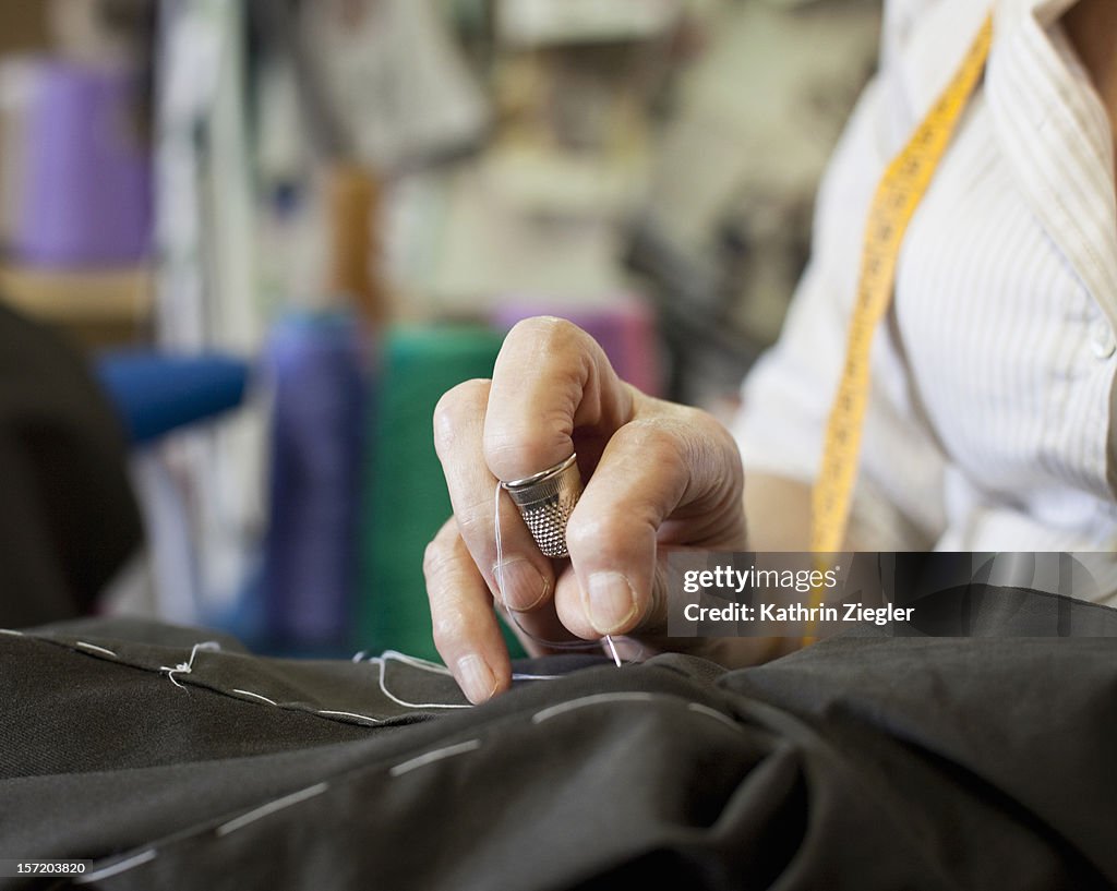 Senior fashion designer sewing, close-up of hands