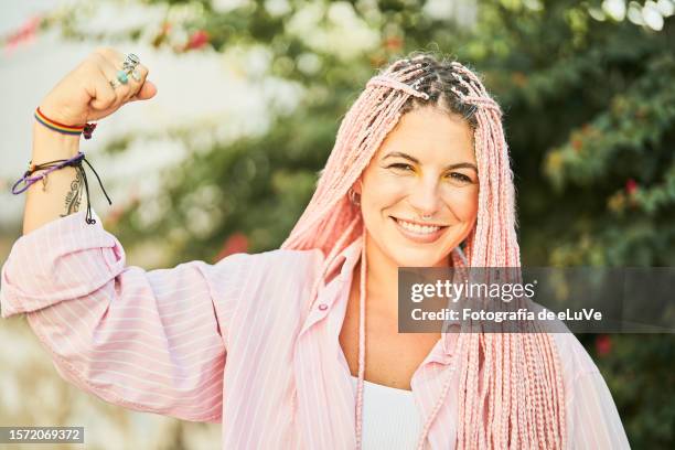 close-up portrait of a pretty young girl with a toothy smile while raising an arm in symbol of strength - cornrow braids stock-fotos und bilder