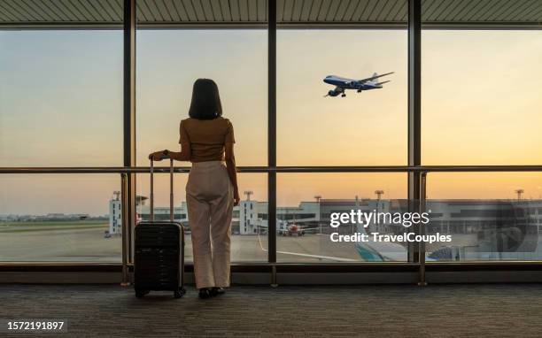 travel tourist standing with luggage watching sunset at airport window. woman looking at lounge looking at airplanes while waiting at boarding gate before departure. travel lifestyle. transport and travel concept - airline seats stock pictures, royalty-free photos & images