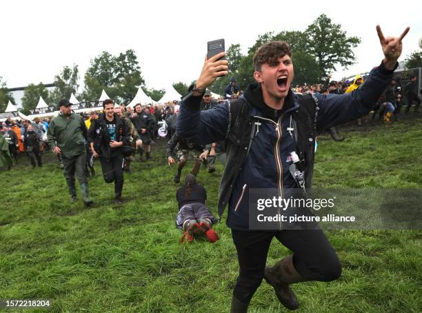 August 2023, Schleswig-Holstein, Wacken: Metal fans run in front of the two main stages on the festival grounds after the opening of the so-called...