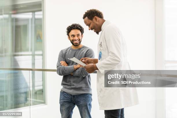 standing together, male doctor smiles and laughs with young man - young men talking stock pictures, royalty-free photos & images