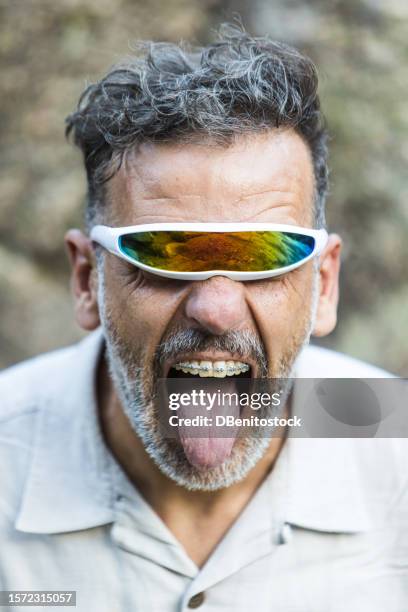 portrait of a mature man with braces wearing futuristic single-lens and mirrored glasses, opening his mouth and sticking out his tongue. concept of dentist, orthodontics, irons, treatment, smile and ugly. - ugly lips stock pictures, royalty-free photos & images