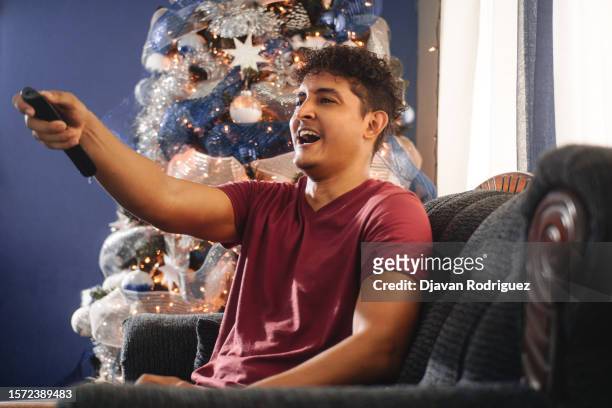 portrait of hispanic young man watching tv. - new broadcasting house stock pictures, royalty-free photos & images