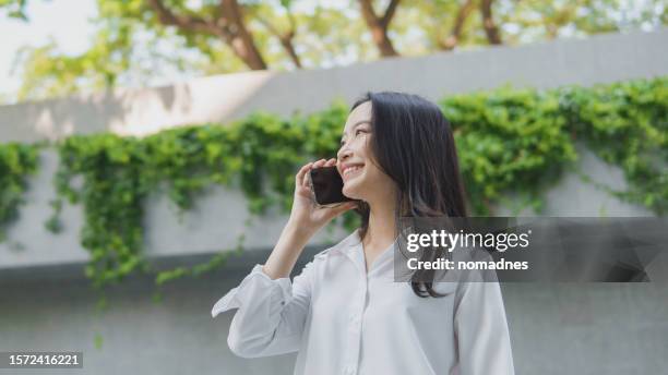 sustainable urban life, asian businesswoman using smartphone with green plant area in urban city background. positive emotion women wear white shirt collars and casual clothing relaxation weekend. - business woman plain background stock pictures, royalty-free photos & images