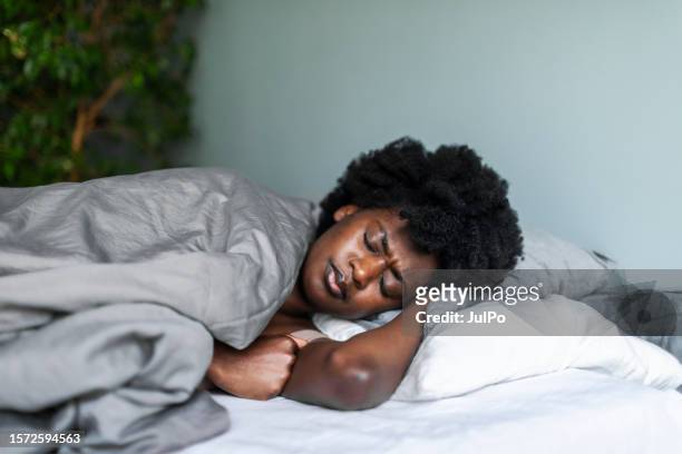 tired frowing young adult black woman with headache lying in bed - woman sleeping stock pictures, royalty-free photos & images