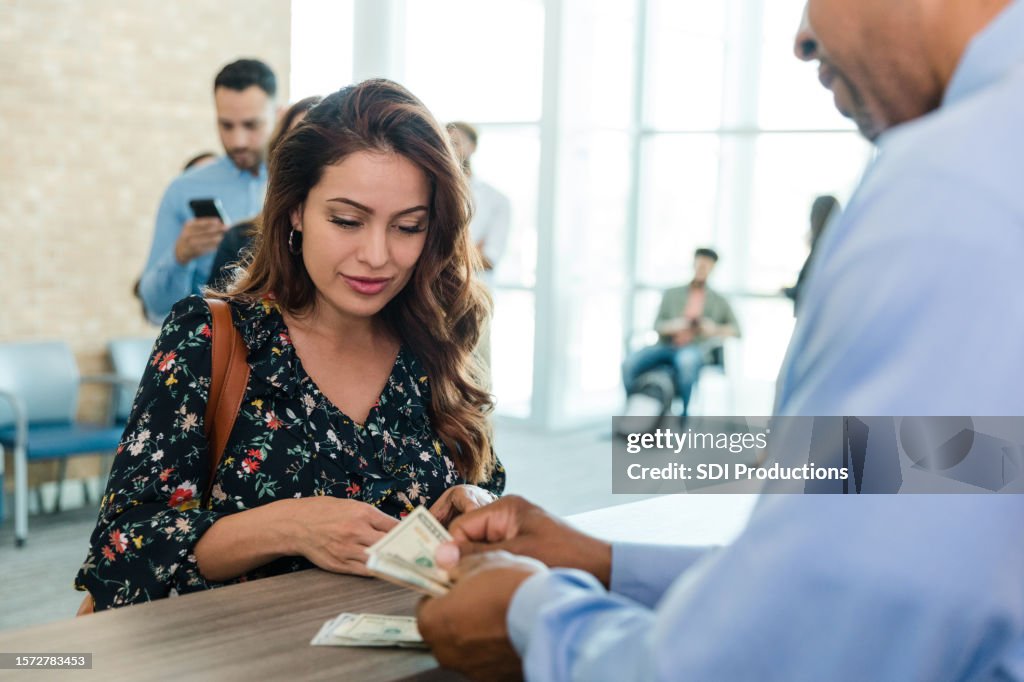 Mid adult woman watches and listens as the unrecognizable bank teller counts her money