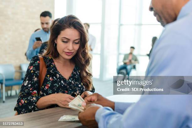 mid adult woman watches and listens as the unrecognizable bank teller counts her money - bank teller stock pictures, royalty-free photos & images