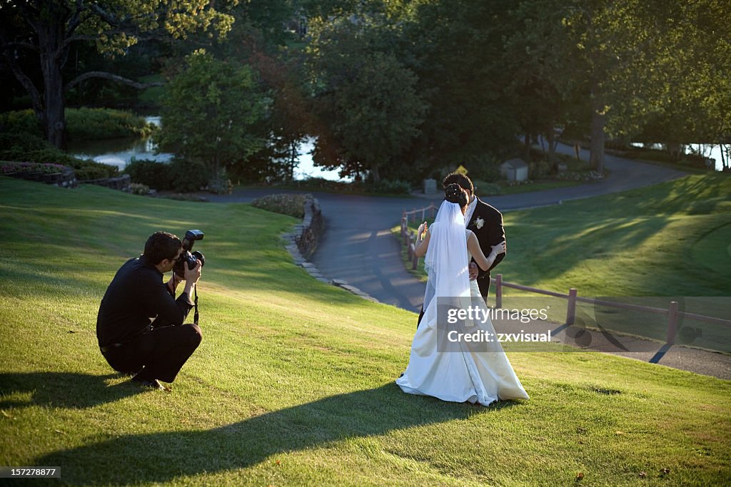 A man taking a photo of a bride and groom missing in grass