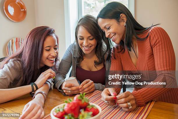 smiling mom and daughters looking at smartphone - three people at table stock pictures, royalty-free photos & images