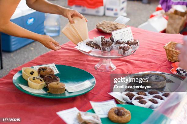 woman offers fresh pastry at charity fundraiser bake sale - bran muffin stock pictures, royalty-free photos & images