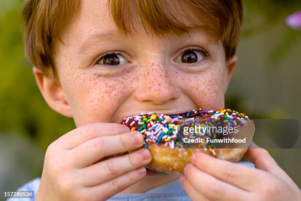 boy over eating chocolate donut, child snacking on unhealthy food - eating donuts stockfoto's en -beelden