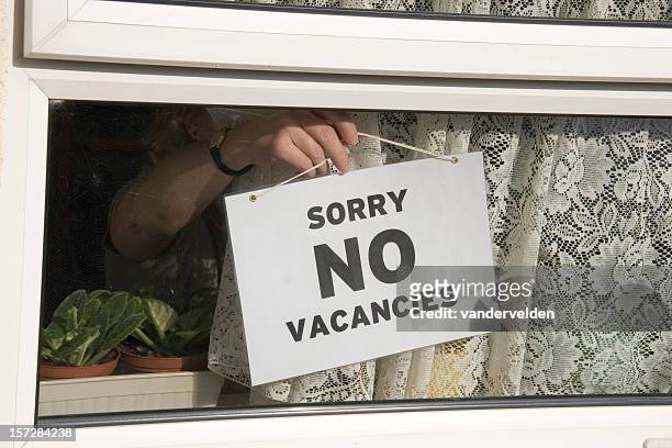 close-up of person hanging no vacancies sign on window - no vacancies stock pictures, royalty-free photos & images