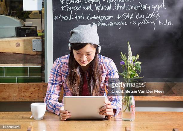 woman with earphones looking at tablet computer in urban cafe - cafe culture uk stock pictures, royalty-free photos & images