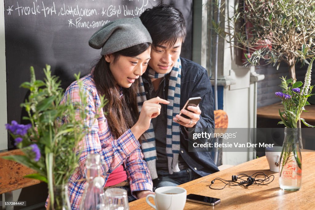 Asian couple looking at the mobile phone in cafe.