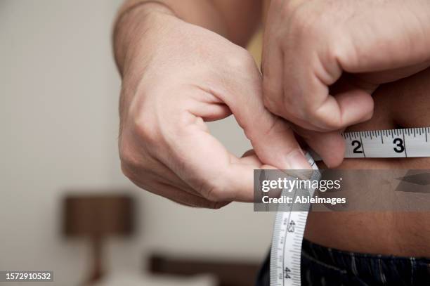 close up of man measuring waist with tape measure - abspecken stock-fotos und bilder