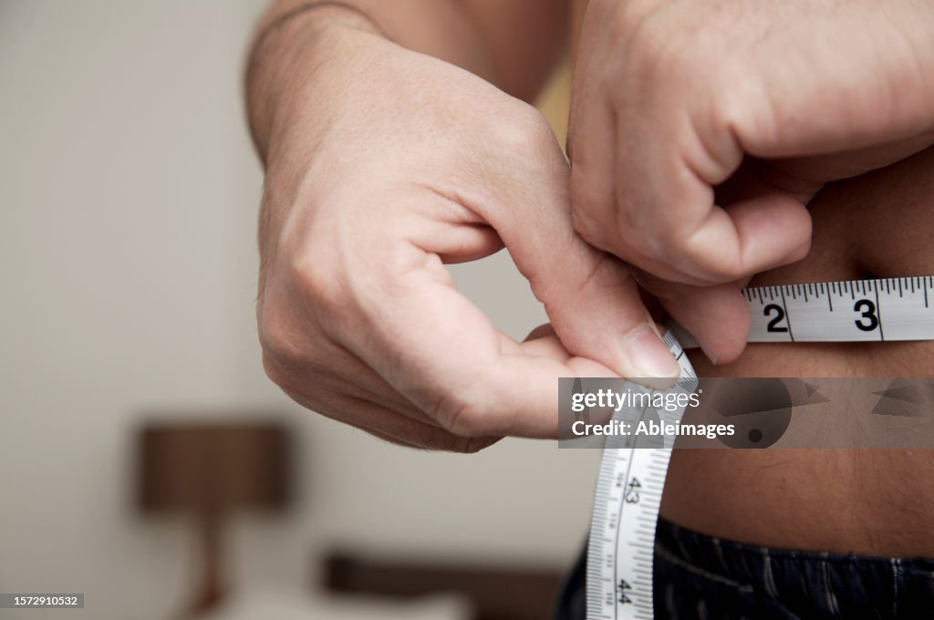 Close up of man measuring waist with tape measure