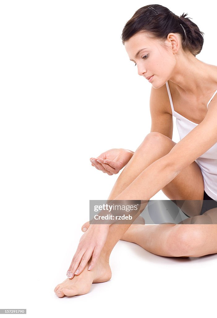 Young woman looking down putting moisturizer on leg