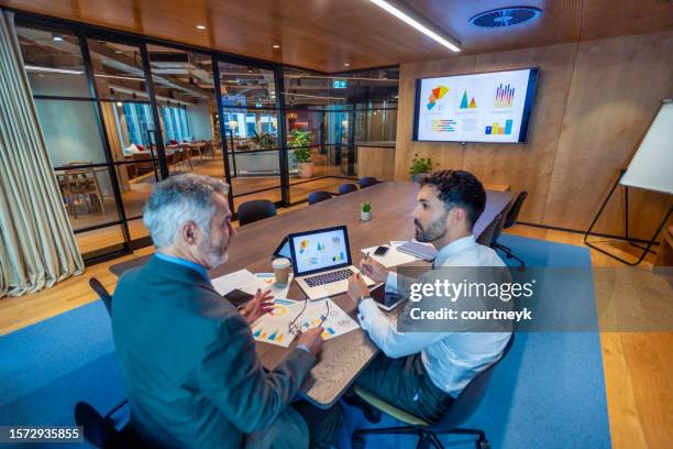 deux hommes d’affaires réunis dans une salle de réunion. il y a de la technologie et des documents sur la table de conférence, y compris un ordinateur portable - accounting services photos et images de collection