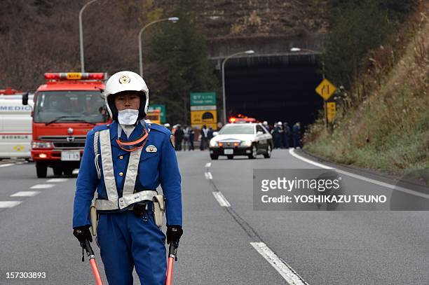 Policeman stands guard in front of emergency service vehicles on the road leading to the entrance of the collapsed Sasago tunnel on the Chuo...