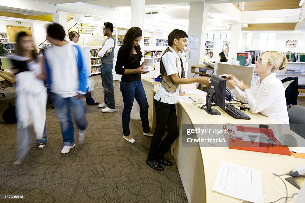 Further education: candid college library scene with librarian helping pupils