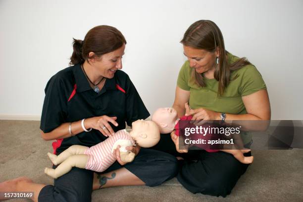 two woman hold baby dummies so they can learn cpr - cpr stock pictures, royalty-free photos & images