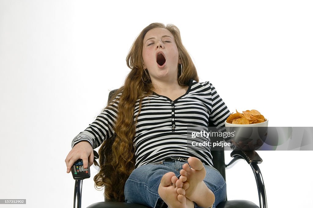 Yawning teenage redhead in chair with crisps and remote control