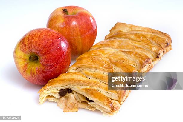 cut open apple strudel next to two whole red apples. - strudel stock pictures, royalty-free photos & images