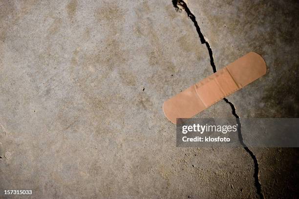 crack in concrete with band-aid on top - stability stock pictures, royalty-free photos & images