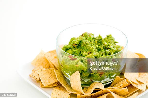 a clear glass bowl of guacamole surrounded by tortilla chips - guacamole isolated stock pictures, royalty-free photos & images