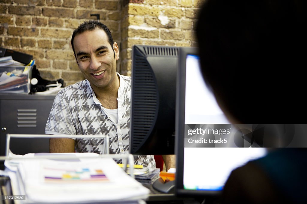Adult male smiling at colleague from behind a computer
