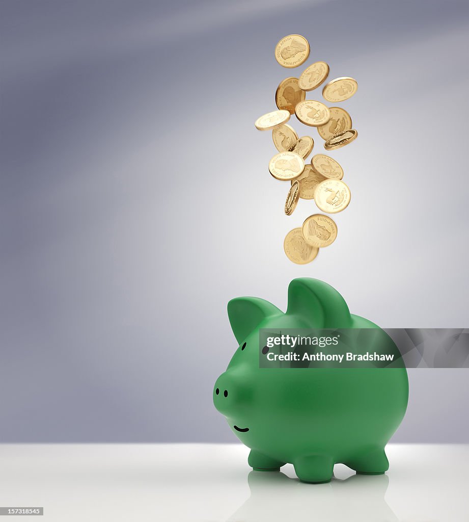Gold coins falling into a green piggy bank