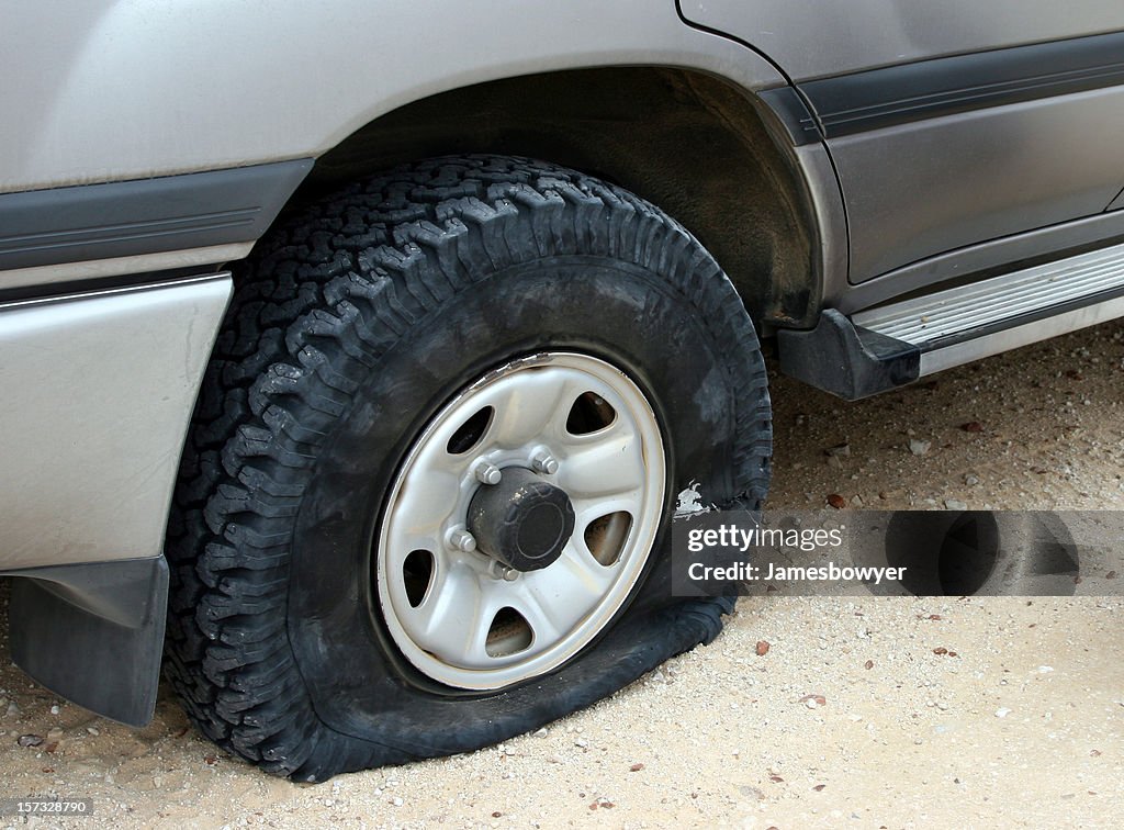 A flat tire deflating on an unpaved road