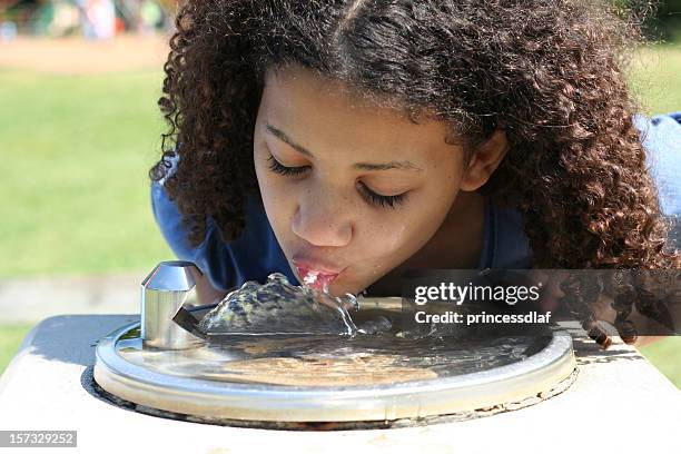 a girl taking a sip from a water dispenser at a park - african girl drinking water stockfoto's en -beelden