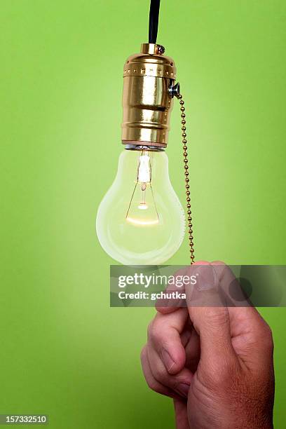 hand pulling chain to turn off light bulb green background - turn off light stock pictures, royalty-free photos & images