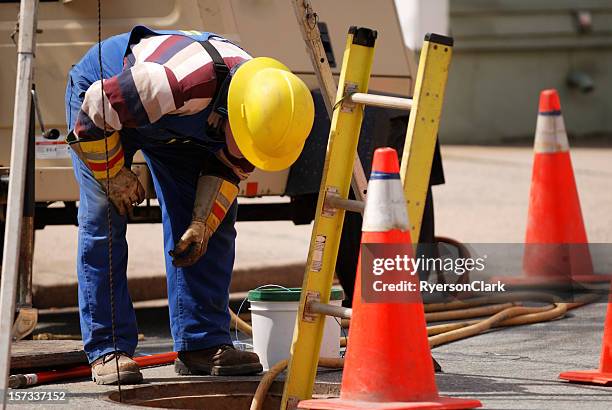 construction worker looking down man hole. - manhole construction stock pictures, royalty-free photos & images
