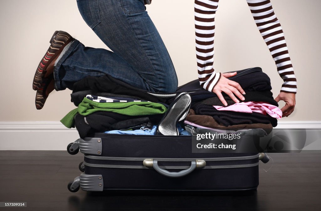 Image of woman kneeing on overfilled luggage to close it