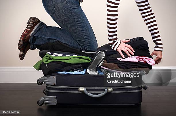 image of woman kneeing on overfilled luggage to close it - stuffing stock pictures, royalty-free photos & images
