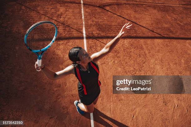 professional tennis player serves on clay court - female tennis player stock pictures, royalty-free photos & images