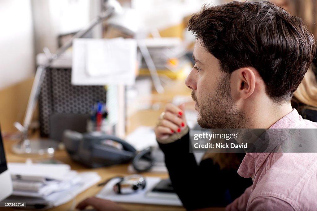 Young man sitting at his desk working on a computer in an office environment