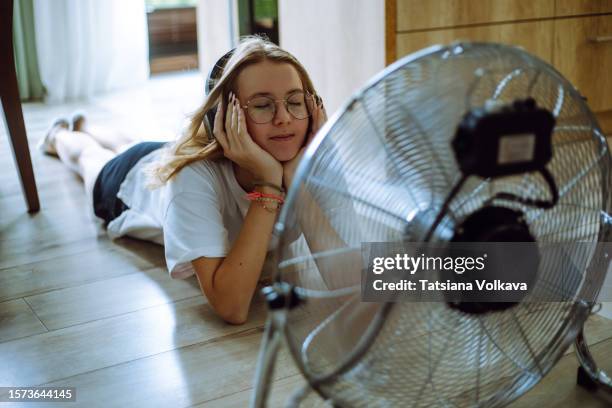 sonic oasis: a teen girl creates her personal oasis on the floor, listening to music through wireless headphones in front of a cooling fan - feber bildbanksfoton och bilder