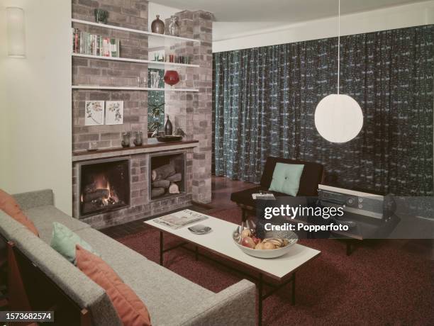 Interior view of a contemporary living room, it contains a sofa and chair, a coffee table, shelves and bookshelves above an open fire and wood...