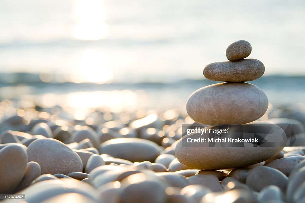 Balanced stones on a pebble beach during sunset.
