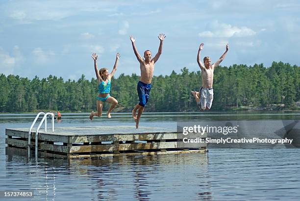 siblings jumping into lake - cottage family stock pictures, royalty-free photos & images