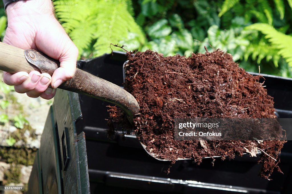 Pala de mano agarrando completo de abono, hogar de compostaje